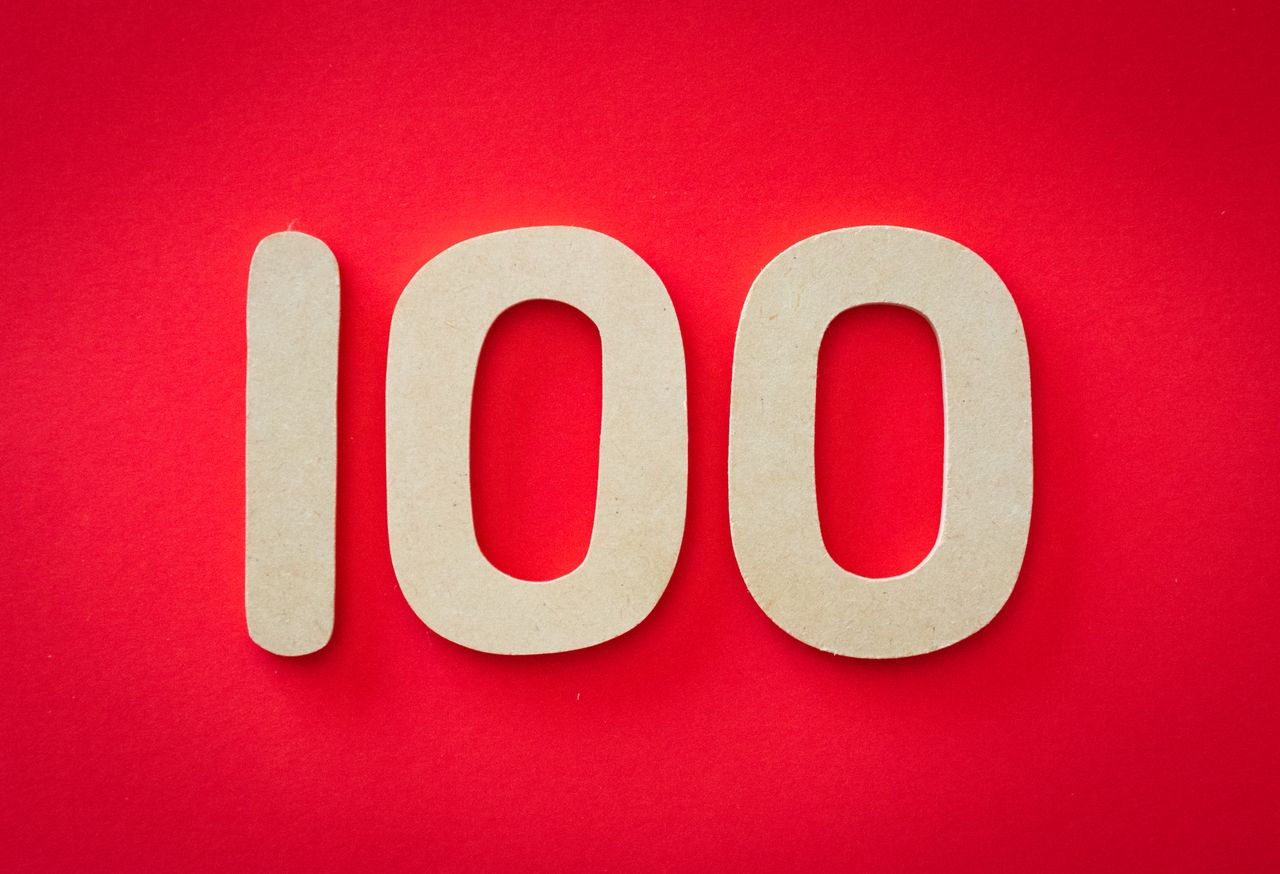 About Close-up of numeral 100 in beige on a bright red background, emphasizing celebration.