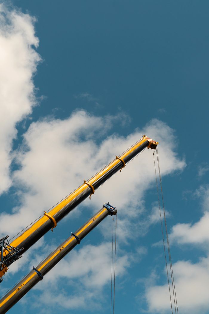 Services Two towering construction cranes extend against a clear blue sky, showcasing industrial power.
