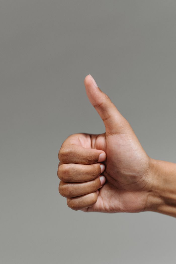 About A close-up of a hand showing a thumbs up gesture, symbolizing success and approval.